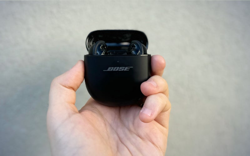 A pesron holding a pair Bose QuietComfort Ultimate against a plain wall.